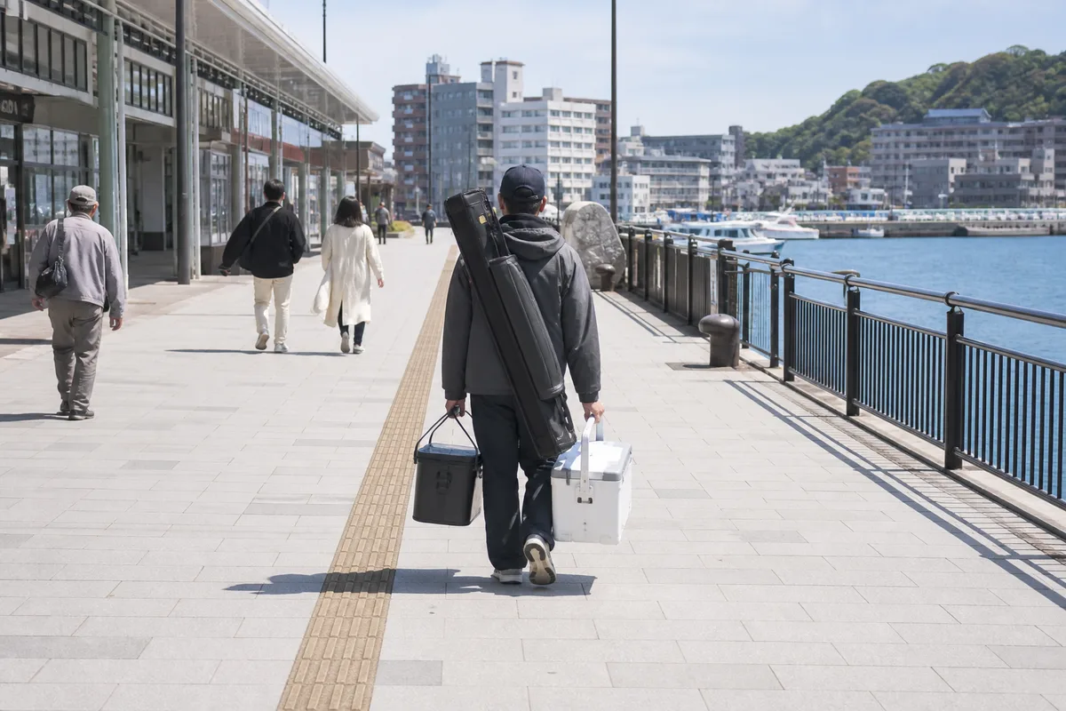 電車釣行で小型バッカンとクーラーを分けて持つ釣り人