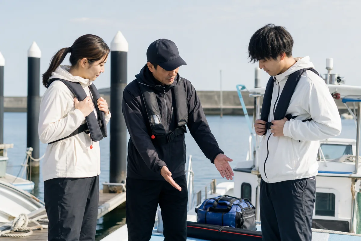 出船前の船着き場で、スタッフの安全説明を聞きながら、同行する初心者同士がライフジャケットと荷物の置き場所を確認している