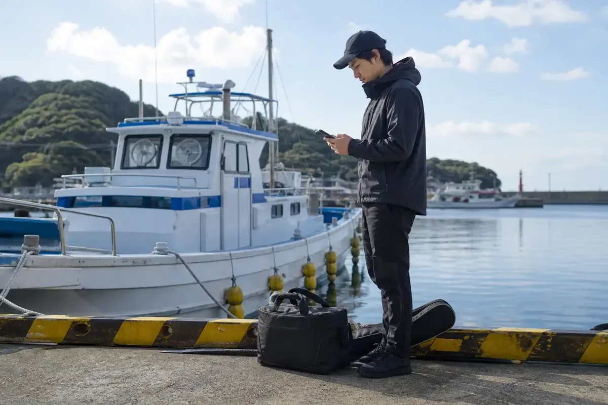 港でスマートフォンを見ながらマハタ船の準備を確認する釣り人