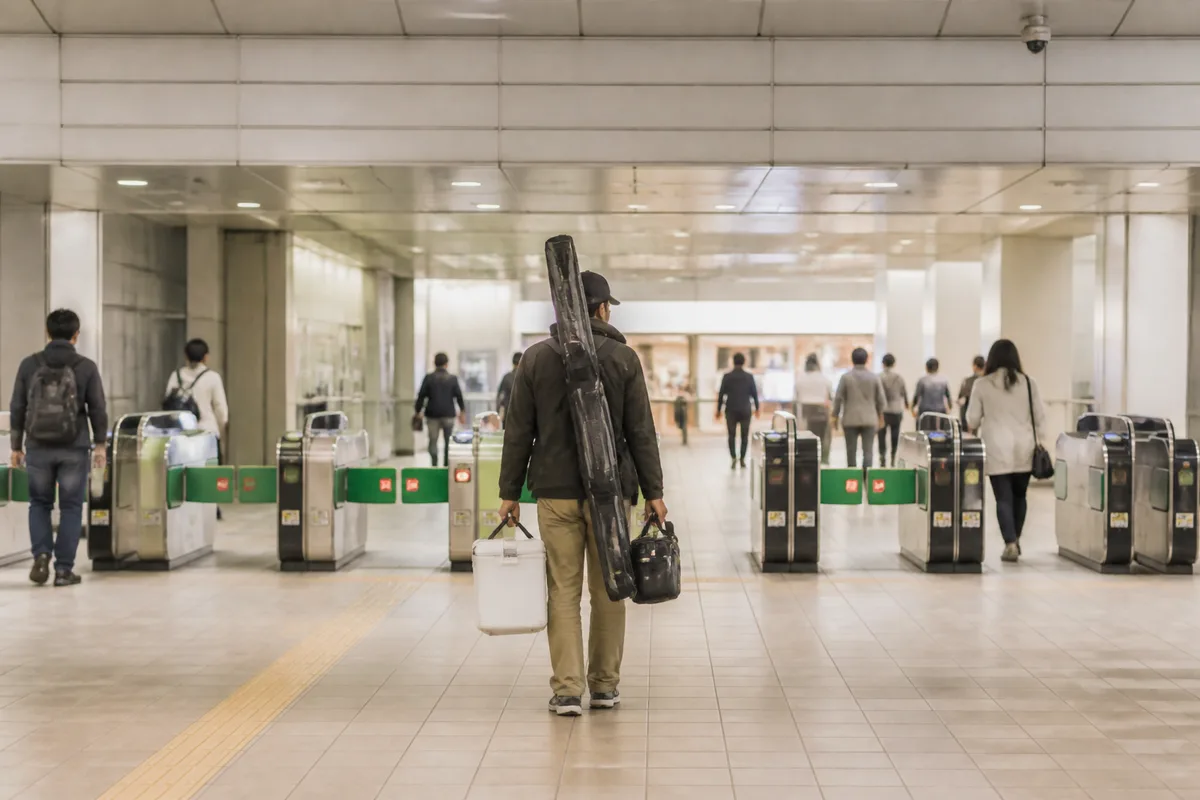 駅の改札前でロッドケースを体の前に寄せて持っている釣り人